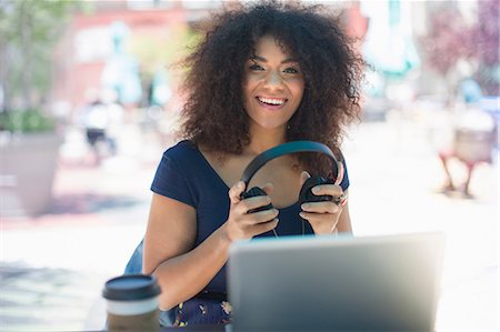 portable computer - Young woman holding headphones at sidewalk cafe Stock Photo - Premium Royalty-Free, Code: 614-07145784