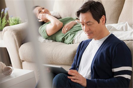 Mature man using digital tablet, woman lying on sofa Foto de stock - Sin royalties Premium, Código: 614-07146194