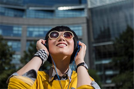 Young woman wearing sunglasses and headphones looking up Stock Photo - Premium Royalty-Free, Code: 614-07146658