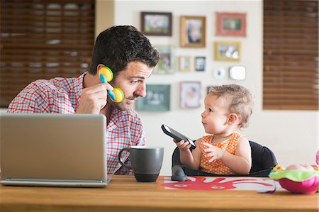Man and baby sitting at kitchen counter playing with smartphone and toy phone Foto de stock - Sin royalties Premium, Código: 614-07194308
