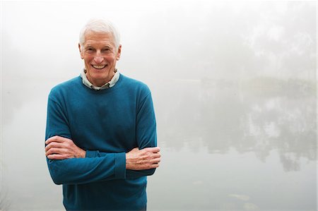 Senior man with arms crossed by foggy lake Stock Photo - Premium Royalty-Free, Code: 614-07234968