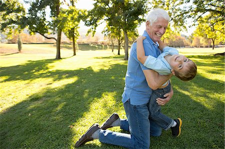 senior family fun outdoor - Grandfather kneeling on grass hugging grandson Stock Photo - Premium Royalty-Free, Code: 614-07235014