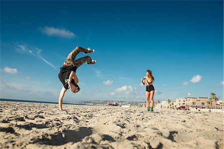 Young woman photographing boyfriend doing backflip on San Diego beach Photographie de stock - Premium Libres de Droits, Code: 614-07240085