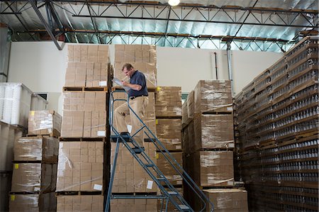 Man on ladders in warehouse with cardboard boxes Photographie de stock - Premium Libres de Droits, Code: 614-07240167