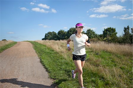 exercising with technology - Young female runner running alongside dirt track Stock Photo - Premium Royalty-Free, Code: 614-07444007