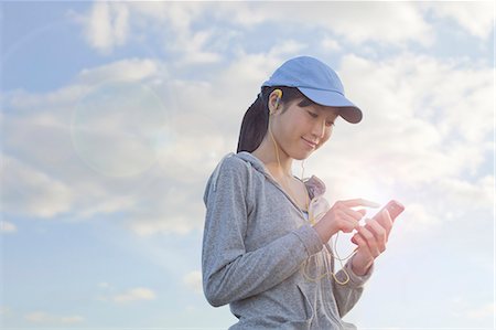 Young female runner choosing music from MP3player Stock Photo - Premium Royalty-Free, Code: 614-07444026