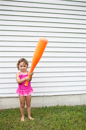 simsearch:614-07444052,k - Female toddler in garden holding a large orange baseball bat Foto de stock - Royalty Free Premium, Número: 614-07444054