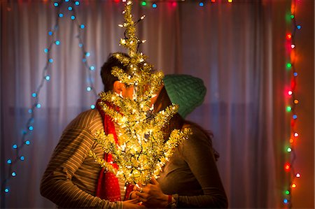 Young couple kissing behind illuminated christmas tree Stock Photo - Premium Royalty-Free, Code: 614-07444167