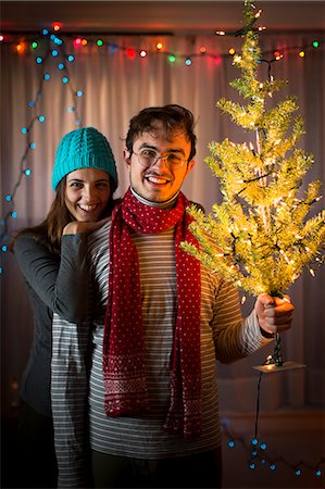 romantic couple in living room - Young couple holding up illuminated christmas tree Stock Photo - Premium Royalty-Free, Code: 614-07444169