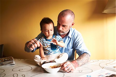 family tattoo - Baby boy sitting on table having cereal with father Stock Photo - Premium Royalty-Free, Code: 614-07444281