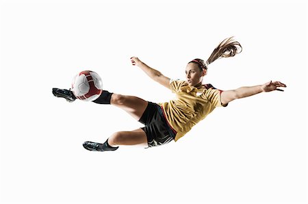 Studio shot of young female soccer player kicking ball mid air Stock Photo - Premium Royalty-Free, Code: 614-07444392