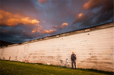 Young man standing next to white wall with his bicycle Stock Photo - Premium Royalty-Free, Code: 614-07487155