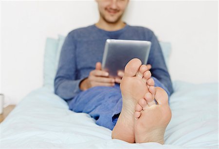 pyjama - Mid adult man lying on bed using digital tablet Photographie de stock - Premium Libres de Droits, Code: 614-07487160