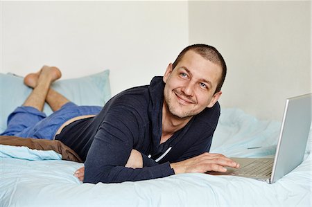 Mid adult man lying on bed using laptop Stock Photo - Premium Royalty-Free, Code: 614-07487162