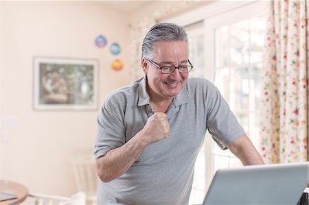 Mature man celebrating whilst looking at laptop Stock Photo - Premium Royalty-Free, Code: 614-07587708