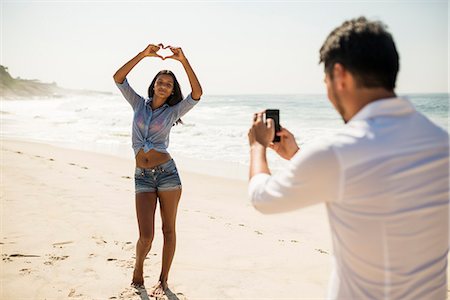 fingers heart - Mid adult man photographing girlfriend on smartphone, Arpoador beach, Rio De Janeiro, Brazil Stock Photo - Premium Royalty-Free, Code: 614-07652224