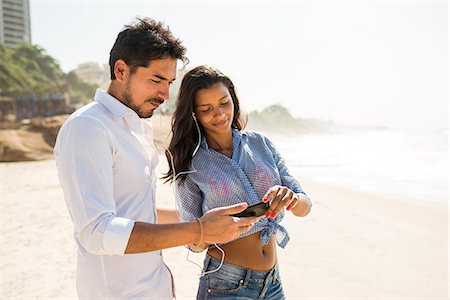 summer clothes - Couple choosing music from smartphone, Arpoador beach, Rio De Janeiro, Brazil Stock Photo - Premium Royalty-Free, Code: 614-07652222