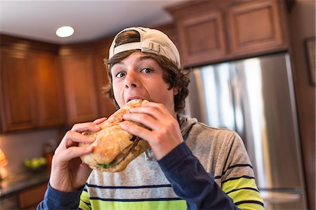 eating at home - Teenage boy in kitchen biting large sandwich Stock Photo - Premium Royalty-Free, Code: 614-07652481