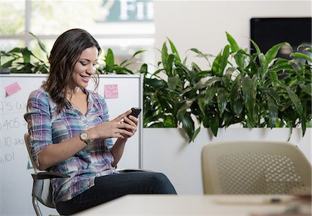 Relaxed young businesswoman texting on smartphone in office Stock Photo - Premium Royalty-Free, Code: 614-07708144