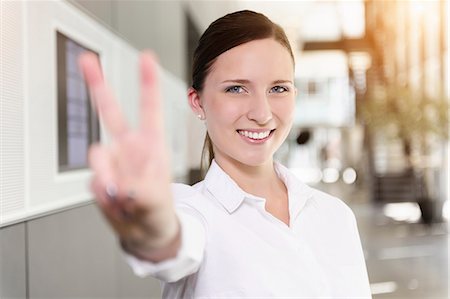Portrait of young businesswoman holding up hand in victory sign Stock Photo - Premium Royalty-Free, Code: 614-07735196
