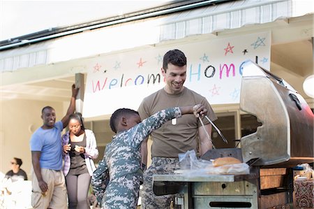 Boy barbecuing burgers with male soldier at homecoming party Stock Photo - Premium Royalty-Free, Code: 614-07735250