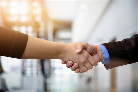 Close up of businesswomen and businessman shaking hands in office Stock Photo - Premium Royalty-Free, Code: 614-07735364