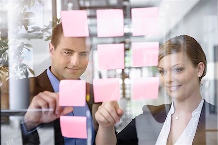 Businessman and woman arranging post it notes on office window Stock Photo - Premium Royalty-Free, Code: 614-07735362