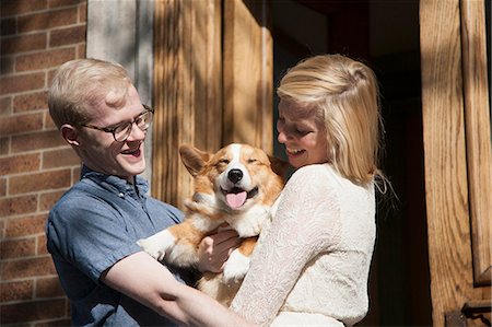 Happy young couple with corgi dog in arms outside front door Stock Photo - Premium Royalty-Free, Code: 614-07735426