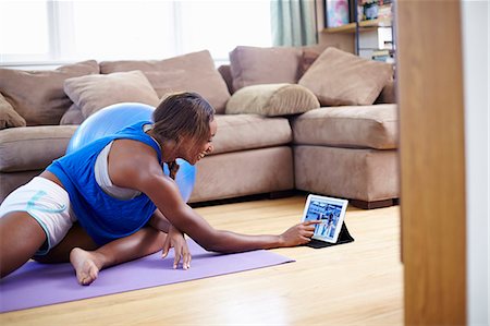 simsearch:614-07735458,k - Young woman exercising on sitting room floor whilst using touchscreen on digital tablet Foto de stock - Sin royalties Premium, Código: 614-07735462