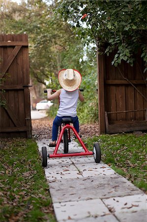 shoeless - Four year old girl riding her tricycle out of garden gate Stock Photo - Premium Royalty-Free, Code: 614-07735499