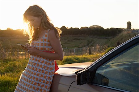 em contraluz - Mid adult woman leaning against car texting on smartphone Foto de stock - Royalty Free Premium, Número: 614-07735523