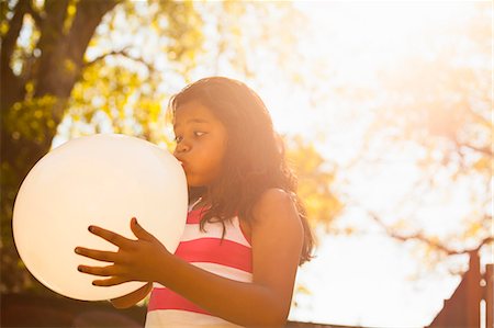 preteen latin girl - Girl blowing up balloon in garden Stock Photo - Premium Royalty-Free, Code: 614-07768068