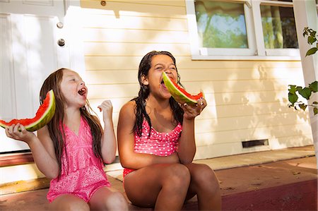 preteen swimsuits - Two laughing girls sitting on house porch with slices of watermelon Stock Photo - Premium Royalty-Free, Code: 614-07768115