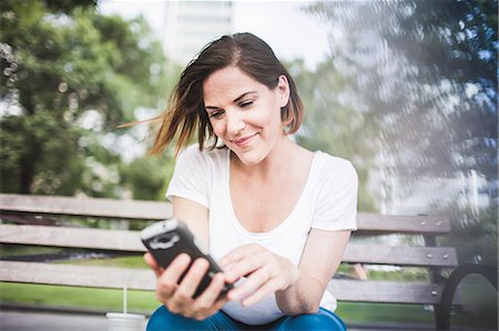 sonrisa - Mid adult woman texting on smartphone in park Foto de stock - Sin royalties Premium, Código: 614-07768234
