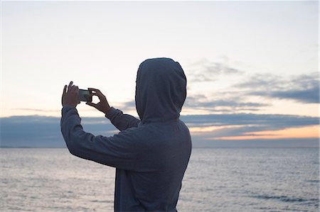Mid adult man in hooded top photographing sea with smartphone, Gloucester, Massachusetts, USA Photographie de stock - Premium Libres de Droits, Code: 614-07768282