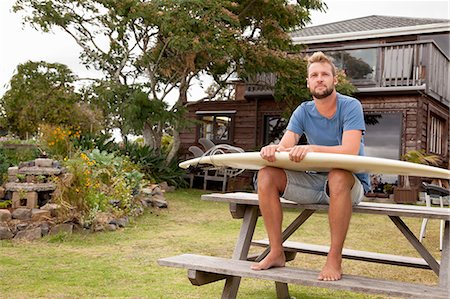 short pants (casual summer wear) - Portrait of male surfer sitting on picnic bench with surfboard on lap Stock Photo - Premium Royalty-Free, Code: 614-07768290