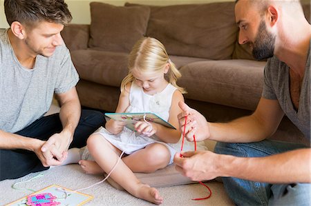 Male couple and daughter threading picture books on sitting room floor Stockbilder - Premium RF Lizenzfrei, Bildnummer: 614-07805891