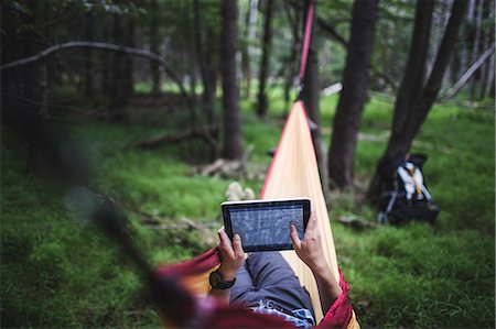 Hiker lying in hammock in forest looking at map on digital tablet Stock Photo - Premium Royalty-Free, Code: 614-07806051