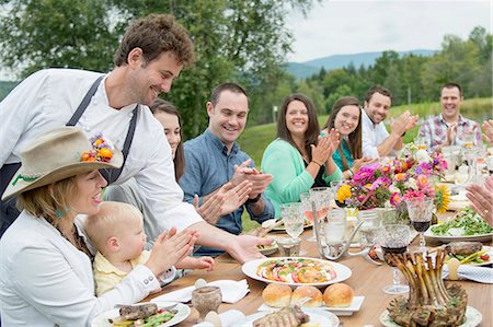 Mid adult man in apron, serving plate of food to family members at table, outdoors Stock Photo - Premium Royalty-Free, Code: 614-07806374