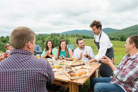 simsearch:614-07806372,k - Mid adult man in apron, serving plate of food to family members at table, outdoors Foto de stock - Sin royalties Premium, Código: 614-07806373