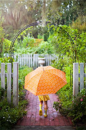 Girl walking through garden gate carrying umbrella Stock Photo - Premium Royalty-Free, Code: 614-07806392