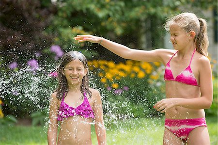 Girls in swimming costume playing with garden sprinkler Stock Photo - Premium Royalty-Free, Code: 614-07806476