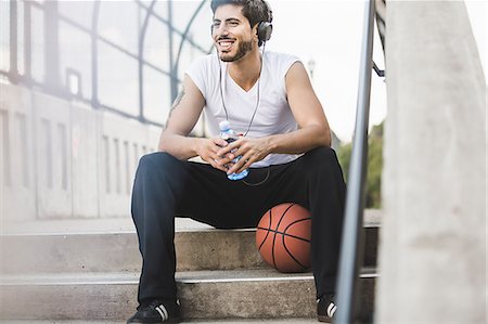 Young male basketball player sitting on footbridge listening to headphones Photographie de stock - Premium Libres de Droits, Code: 614-07911680