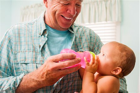 Grandfather bottle feeding baby granddaughter on lap in living room Photographie de stock - Premium Libres de Droits, Code: 614-07911721