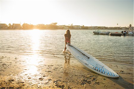 simsearch:614-07911744,k - Young woman lifting paddleboard onto beach at sunset, Mission Bay, San Diego, California, USA Photographie de stock - Premium Libres de Droits, Code: 614-07911745