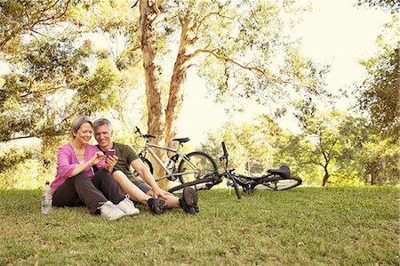 Mature cycling couple sitting in park looking at smartphone Stock Photo - Premium Royalty-Free, Code: 614-07911938