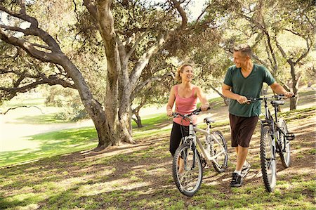 simsearch:614-08220131,k - Mature couple chatting and pushing bicycles through park Photographie de stock - Premium Libres de Droits, Code: 614-07911942