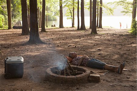 Man lying down next to campfire in forest, Arkansas, USA Fotografie stock - Premium Royalty-Free, Codice: 614-07912008