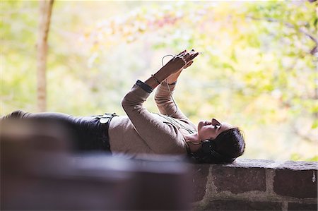Young woman lying on wall holding up smartphone whilst listening to headphones Photographie de stock - Premium Libres de Droits, Code: 614-07912015