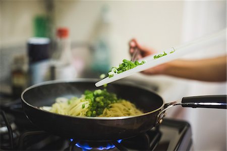 Young woman pouring shopped spring onions into frying pan Stock Photo - Premium Royalty-Free, Code: 614-08000225